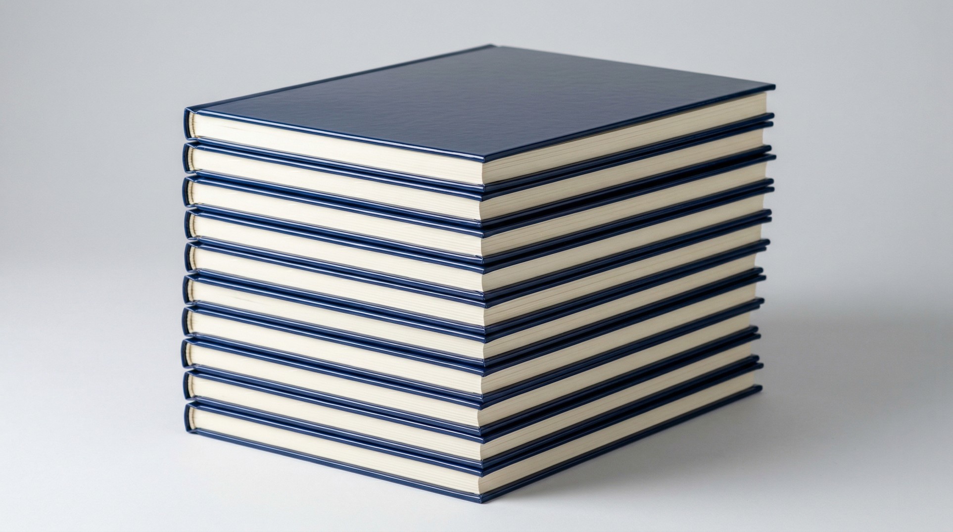 Stack of ten custom hardcover coffee table books with matching navy glossy-laminated covers showing a bulk photo book printing run
